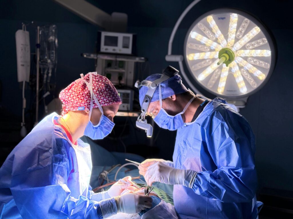 A surgeon controls robotic arms from a console during a long-distance telesurgery procedure.
